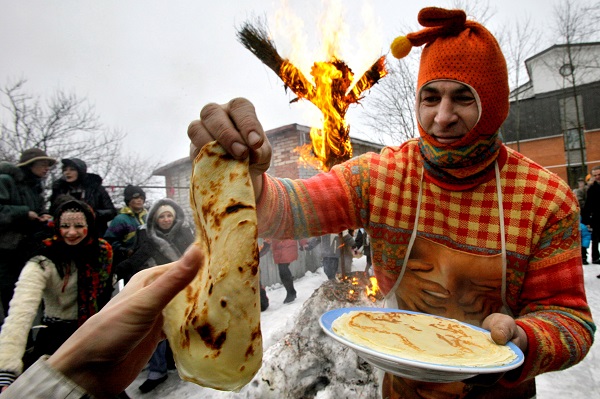 A man dressed as a medieval East Slavic harlequin distributes blini in St. Petersburg, Russia, during the last day of Maslenitsa.Behinde a small effigy of Lady Maslenitsa was burned. 